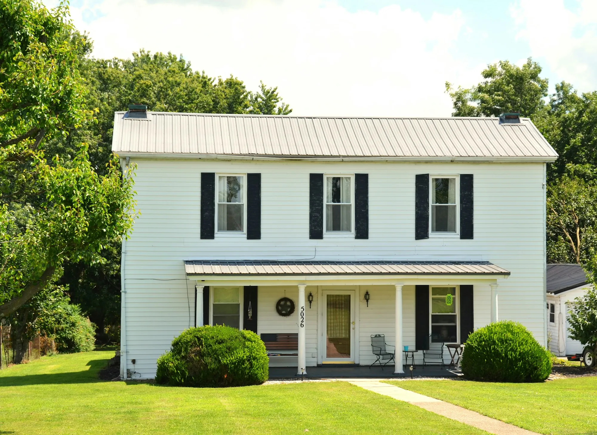 White two-story farmhouse with black shutters and a front porch